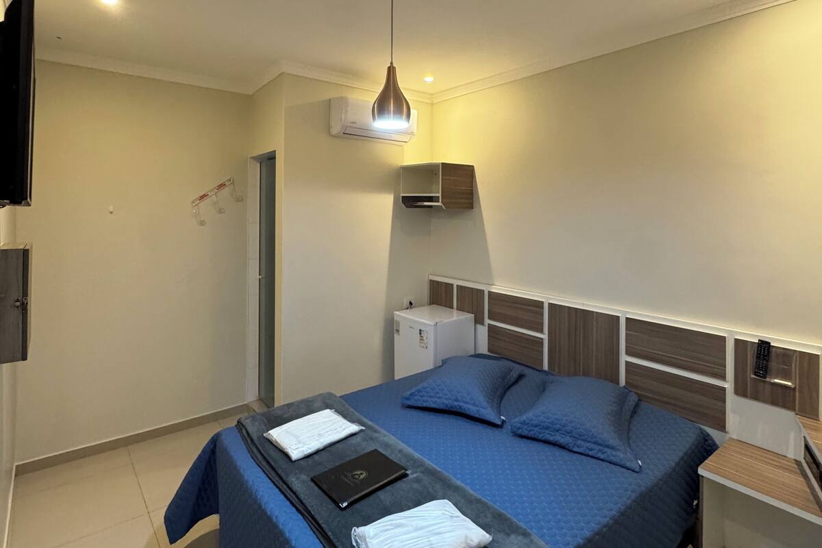 A bedroom with a bed, a desk, a chair, a TV, and an air conditioning unit.