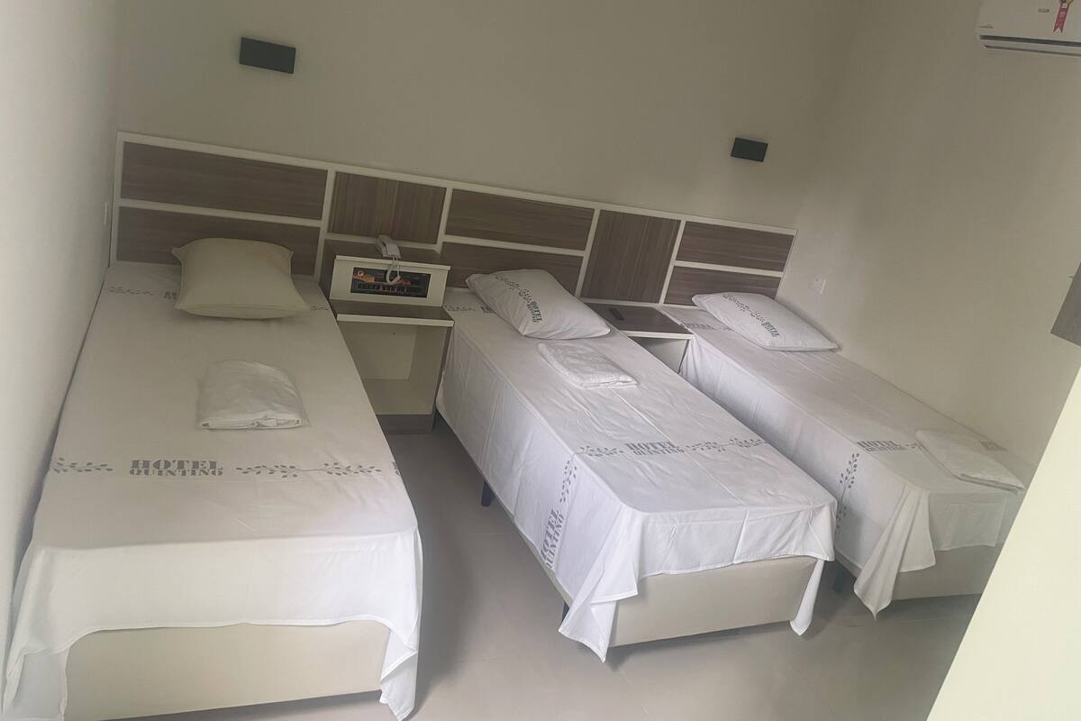 A hotel room with three single beds, a small bedside table with a phone, and a wall-mounted air conditioning unit.