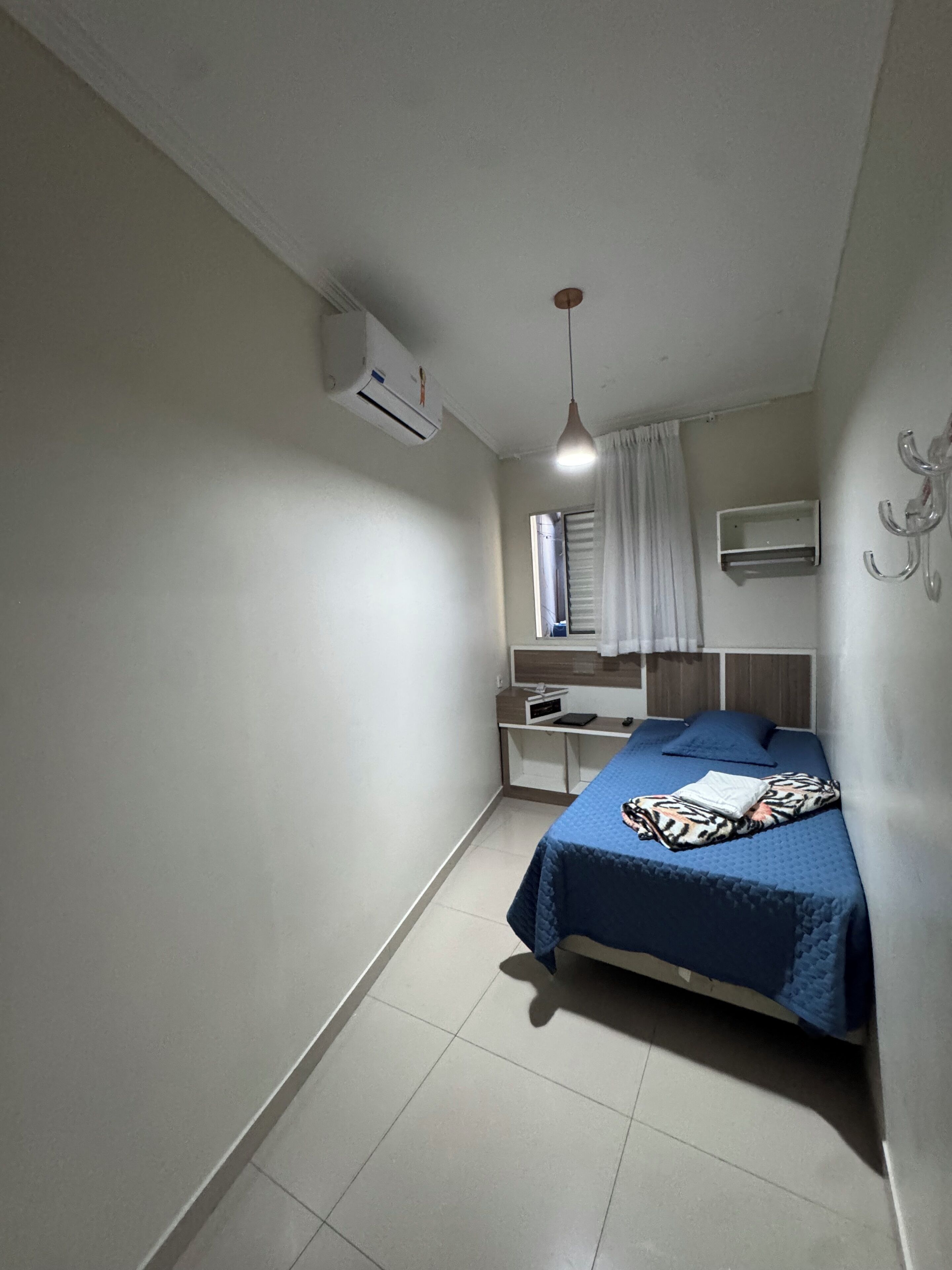 Un dormitorio con cama, escritorio, silla, aire acondicionado y lámpara colgante.