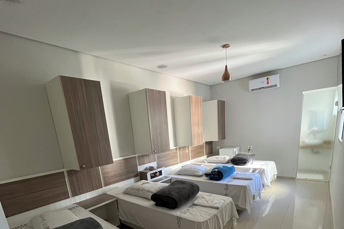 A hotel room with three beds, a minibar, a ceiling fan, and a window with a view.