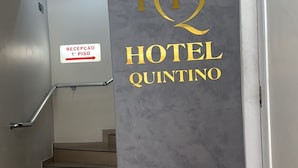 A hotel entrance with a reception desk, a staircase, and a sign indicating the first floor. - Hotel Quintino (São Paulo)