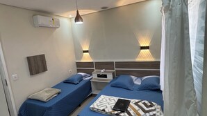 A room with two beds, a bedside table, an air conditioning unit, and a hanging light fixture. - Hotel Quintino (São Paulo)