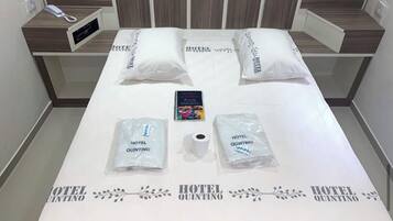 A neatly made hotel bed with pillows, a remote control, and two bags labeled "Hotel Quintino".