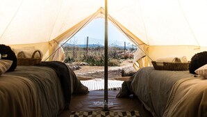 A tent with two beds, each with pillows and a basket. The tent has a pole in the center. - Nomada Glamping - San Miguel de Allende X NANTLI LIVING (San Miguel de Allende)