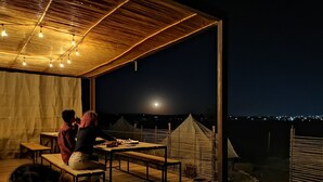 An outdoor dining area with tables and chairs, a wooden ceiling, and a view of the city at night. - Nomada Glamping - San Miguel de Allende X NANTLI LIVING (San Miguel de Allende)