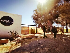 Una persona montando a caballo cerca de un letrero que dice 'NOMADA GLAM-CAMP'.