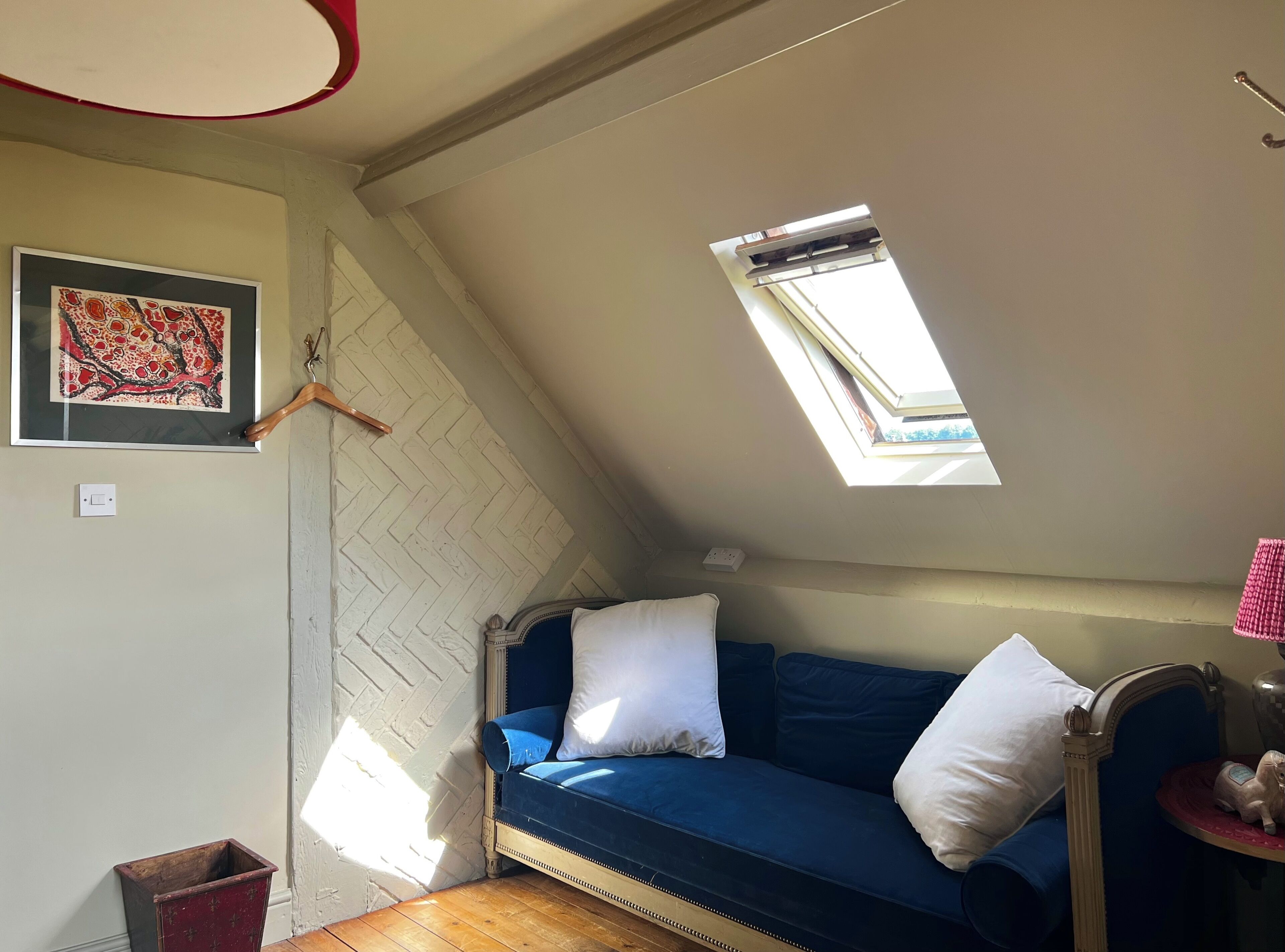 Ein gemütlicher Raum mit schrägen Wänden, einem blauen Sofa mit weißen Kissen, einem kleinen Tisch mit einer Figur und einem gerahmten Kunstwerk an der Wand.