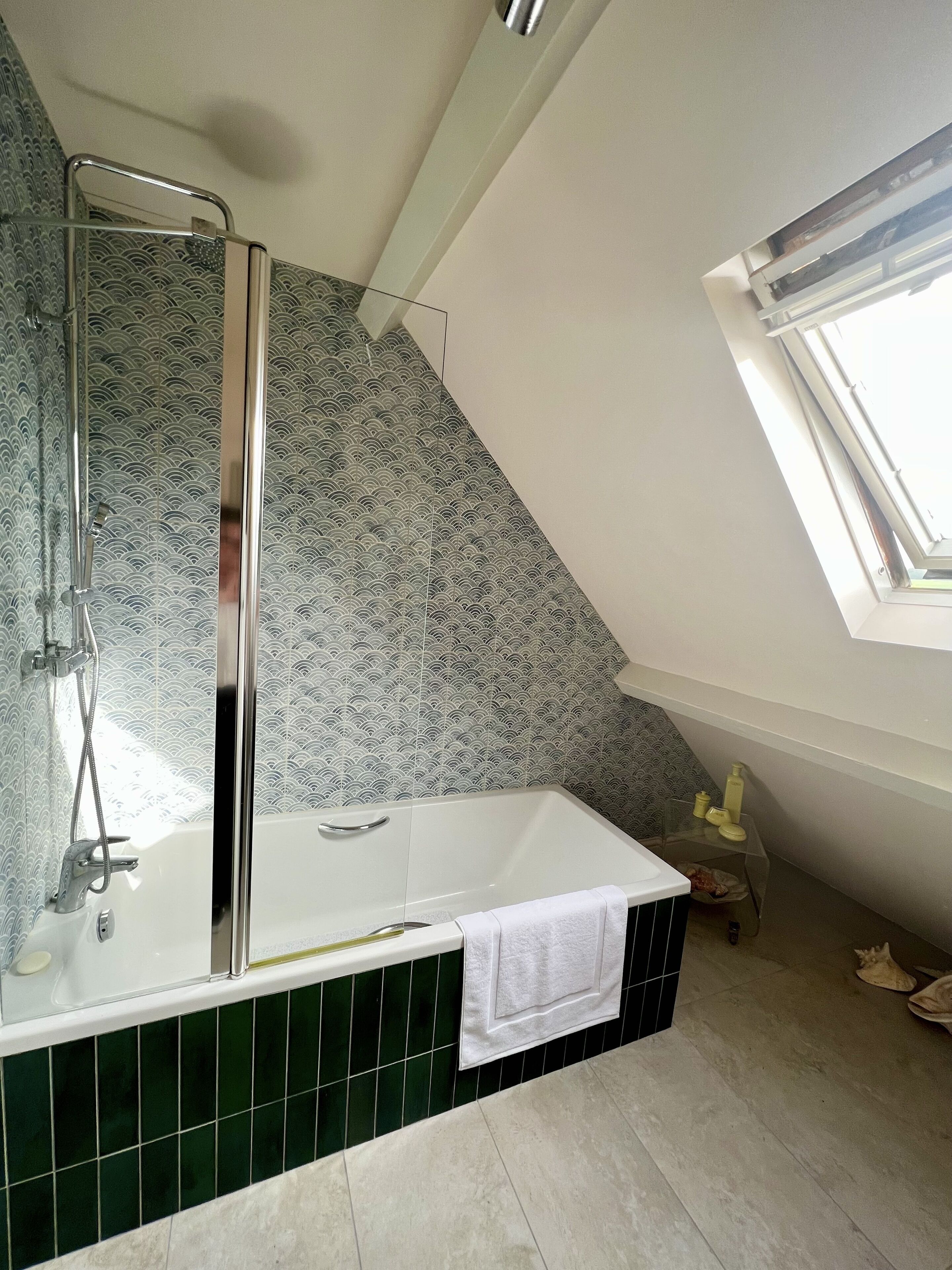 A modern bathroom with a glass-enclosed shower, green tiles, and a skylight.