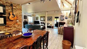 A spacious living area with a dining table, chairs, and a kitchen in the background. - Eclectic Barn · Pergola & Dog-Friendly Garden (Calne)