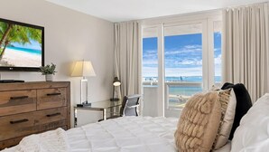 A hotel room with a bed, a desk, a chair, a TV, and a view of the beach. - Bay Overlooking Condo | Downtown | StayCozy (Miami)