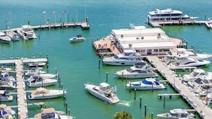 A marina with multiple yachts docked at piers, a building with a flat roof, and a clear blue sky. - Bay View High-Rise | Private Balcony | StayCozy (Miami)