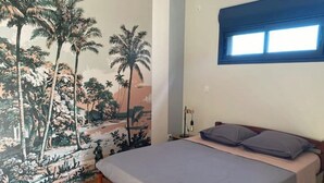 Un dormitorio con cama, mesita de noche, lámpara y ventana.
