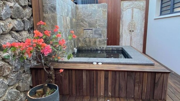 Un área de spa con pared de piedra, terraza de madera y bañera de hidromasaje.