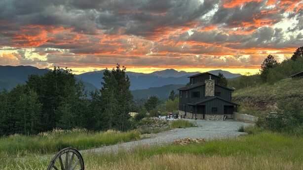 A modern house with a stone chimney, surrounded by a gravel driveway and lush greenery. -  Off Grid Mountain Retreat w/ Amazing Views (Idaho Springs)
