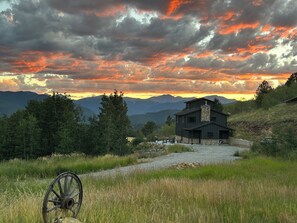 A modern house with a stone chimney, surrounded by a gravel driveway and lush greenery. - Off Grid Mountain Retreat w/ Amazing Views (Idaho Springs)