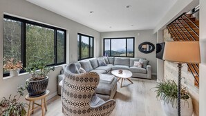 A modern living room with a sectional sofa, a patterned armchair, a small round table, and a large potted plant. -  Off Grid Mountain Retreat w/ Amazing Views (Idaho Springs)