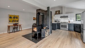 A modern kitchen with a wood-burning stove, a dining area with a table and chairs, and a yellow artwork on the wall. -  Off Grid Mountain Retreat w/ Amazing Views (Idaho Springs)