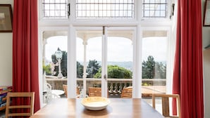 Ein Essbereich mit Tisch und Stühlen, ein Blick durch große Fenster und ein Balkon mit Gartenmöbeln.