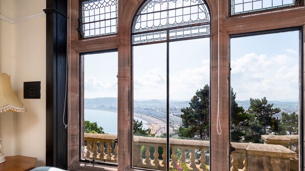 Ein Zimmer mit großen Fenstern und Blick auf eine Küstenstadt und Berge.