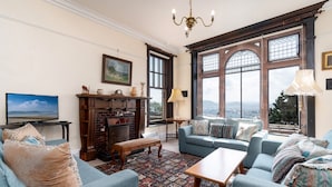 Ein Wohnzimmer mit Kamin, blauen Sofas, einem gemusterten Teppich und großen Fenstern mit Aussicht.