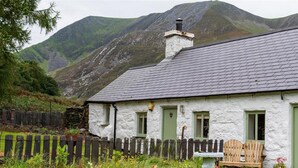 A white house with a grey roof, a wooden fence, and a stone chimney. - Ceunant Bach - One Bedroom Cottage, Sleeps 2 (Bethesda)