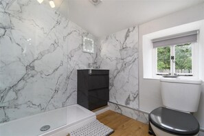 A bathroom with marble walls, a black cabinet, a toilet, and a window with a view of greenery. - Ceunant Bach - One Bedroom Cottage, Sleeps 2 (Bethesda)