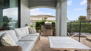 An outdoor patio with a gray sofa, a wooden table, and a stone barbecue grill. - Reunion Resort- Pool, Spa, Game Room, Disney, Golf Course, No resort Fees (Reunion)