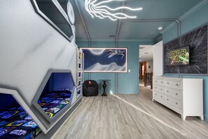 A room with a Star Wars-themed wall art, a Star Wars poster, a bean bag chair, a small table, and a white dresser.