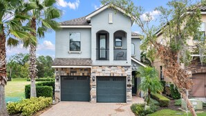 A two-story house with a stone facade, two garage doors, and a small balcony. - Reunion Resort- Pool, Spa, Game Room, Disney, Golf Course, No resort Fees (Reunion)
