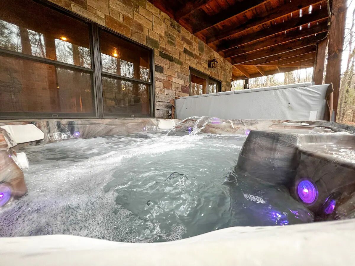 A hot tub with a stone wall backdrop and a wooden ceiling.