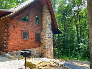 A log cabin with a stone chimney, a porch, and a gravel driveway.