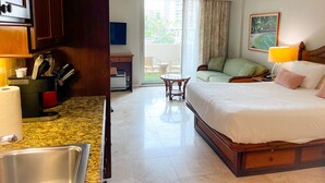 Habitación de hotel con cama, escritorio con silla, una mesita, un sofá y un balcón con vistas a edificios.