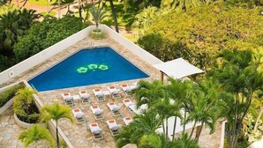 Vista aérea de una piscina rodeada de sillas de descanso y palmeras.