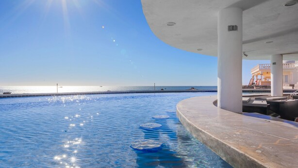 Una piscina con vista diretta sull'oceano e un edificio con tetto curvo.