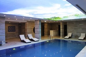 Ein moderner Poolbereich im Innenbereich mit Liegestühlen und einer Wand aus Stein als Hintergrund.