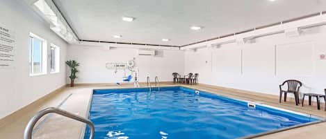 Una piscina interior con agua cristalina, una escalera de metal e iluminación empotrada en el techo.