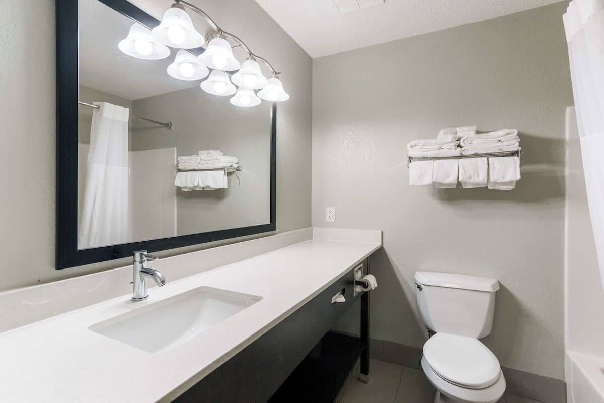 A bathroom with a white sink, a mirror, a toilet, and towel racks.