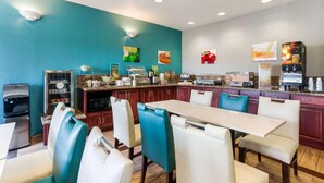 A dining area with a long table, chairs, a refrigerator, a coffee machine, and a microwave. - Quality Inn & Suites Ferdinand (Ferdinand)
