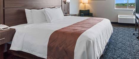 Une chambre d’hôtel avec un grand lit, un bureau, une chaise, une lampe, un tableau et une fenêtre donnant sur un beau paysage.