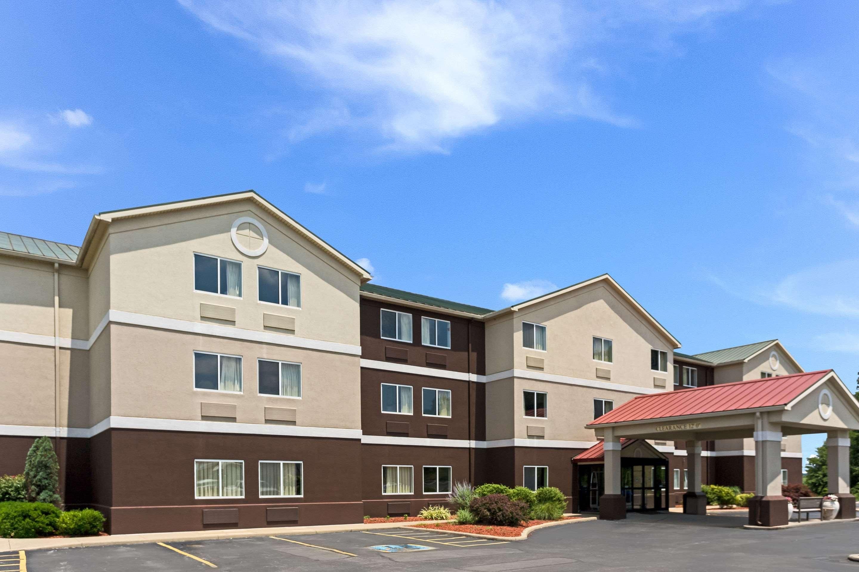 A multi-story hotel with a covered entrance, a parking lot, and a clear blue sky.