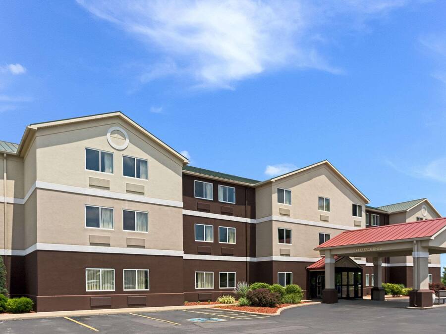 A multi-story hotel with a covered entrance, a parking lot, and a clear blue sky.