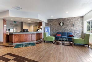 A reception area with a wooden counter, a stone wall, a clock, and a blue sofa. - Quality Inn & Suites Ferdinand (Ferdinand)