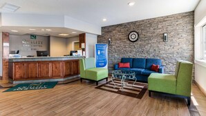 A reception area with a wooden counter, green chairs, a blue sofa, and a stone wall with a clock. - Quality Inn & Suites Ferdinand (Ferdinand)
