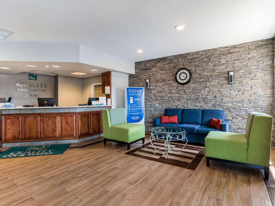 A reception area with a wooden counter, green chairs, a blue sofa, and a stone wall with a clock.