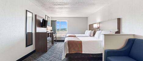 A hotel room with two beds, a desk, a TV, and a view of the outdoors.