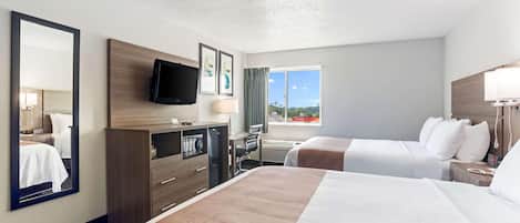 Ein Hotelzimmer mit zwei Betten, einem Schreibtisch mit Stuhl, einem an der Wand befestigten Fernseher und einem großen Fenster mit Blick ins Freie.