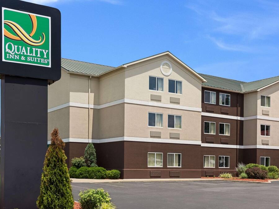 A multi-story hotel with a sign for Quality Inn & Suites, featuring a modern design with a flat roof and a parking lot in front.
