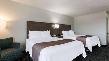 Habitación de hotel con dos camas, una mesita de noche, una lámpara y una silla.