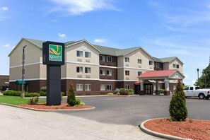 A hotel with a sign reading 'Quality Inn & Suites,' a parking lot, and a building with a red roof. - Quality Inn & Suites Ferdinand (Ferdinand)