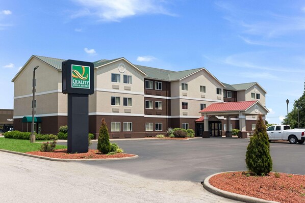 A hotel with a sign reading 'Quality Inn & Suites,' a parking lot, and a building with a red roof. - Quality Inn & Suites Ferdinand (Ferdinand)